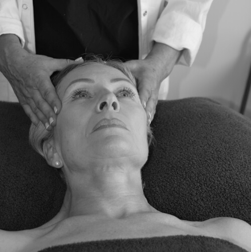 A woman lying on her back on a bed receiving a head massage from Annie Mills